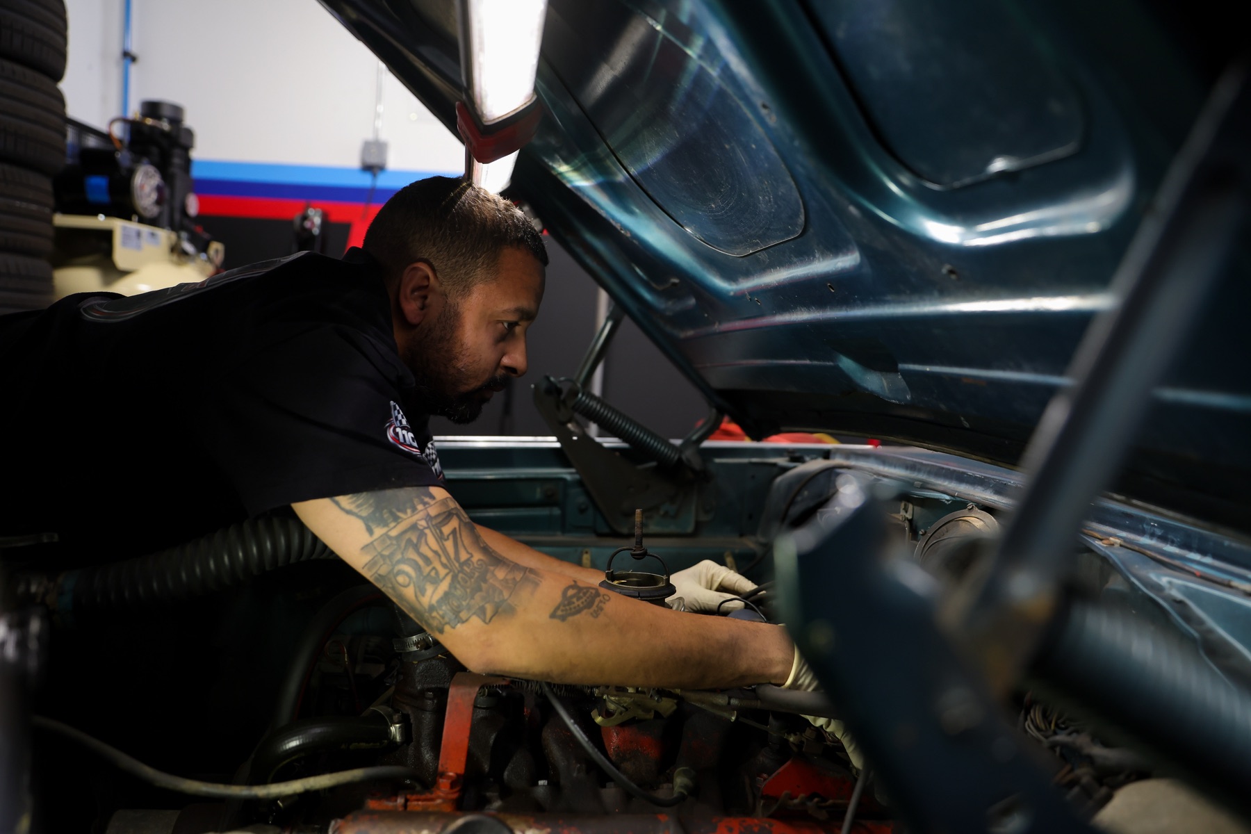 Technician inspecting components inside a classic car engine bay