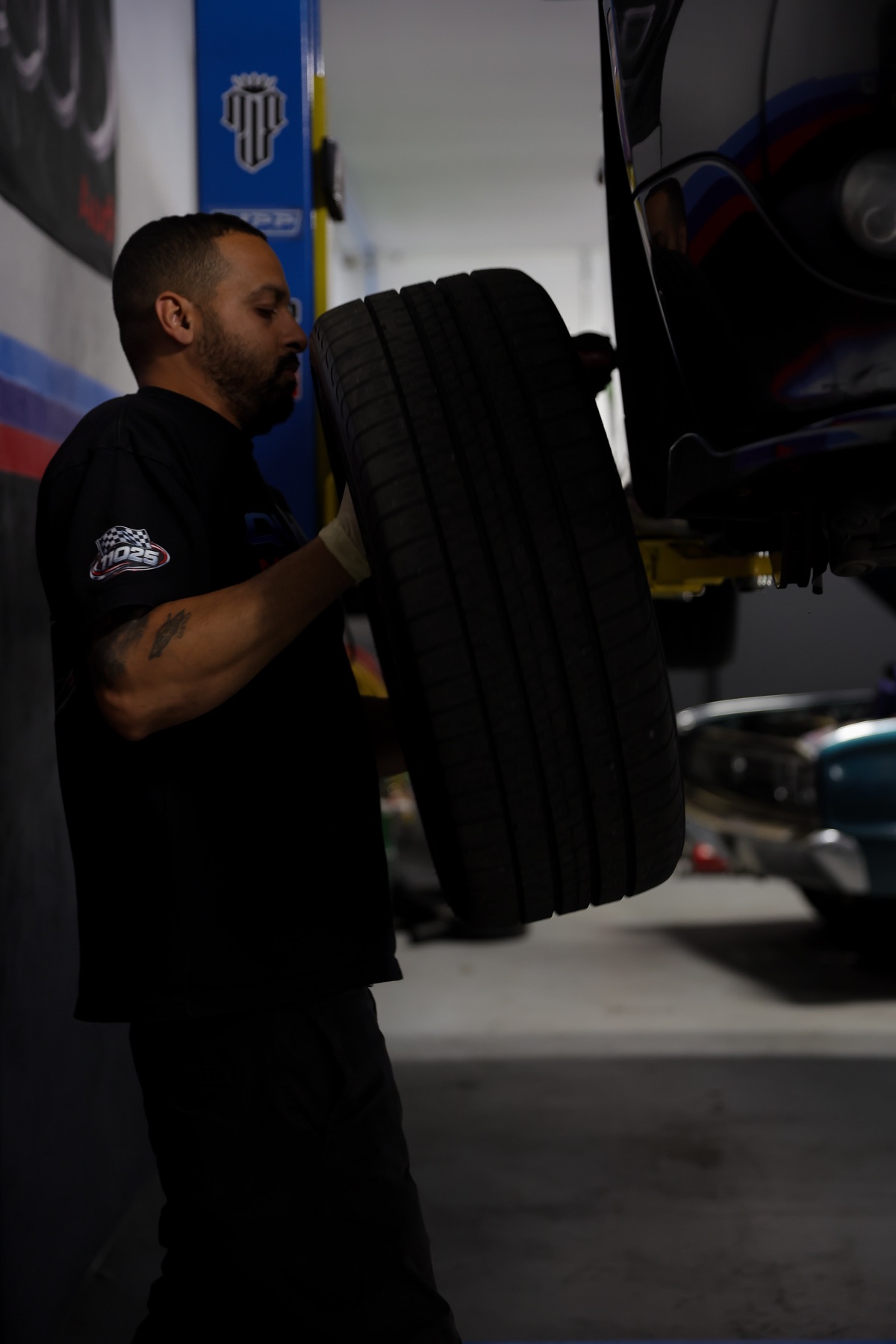 Technician carrying two tires beside a raised vehicle