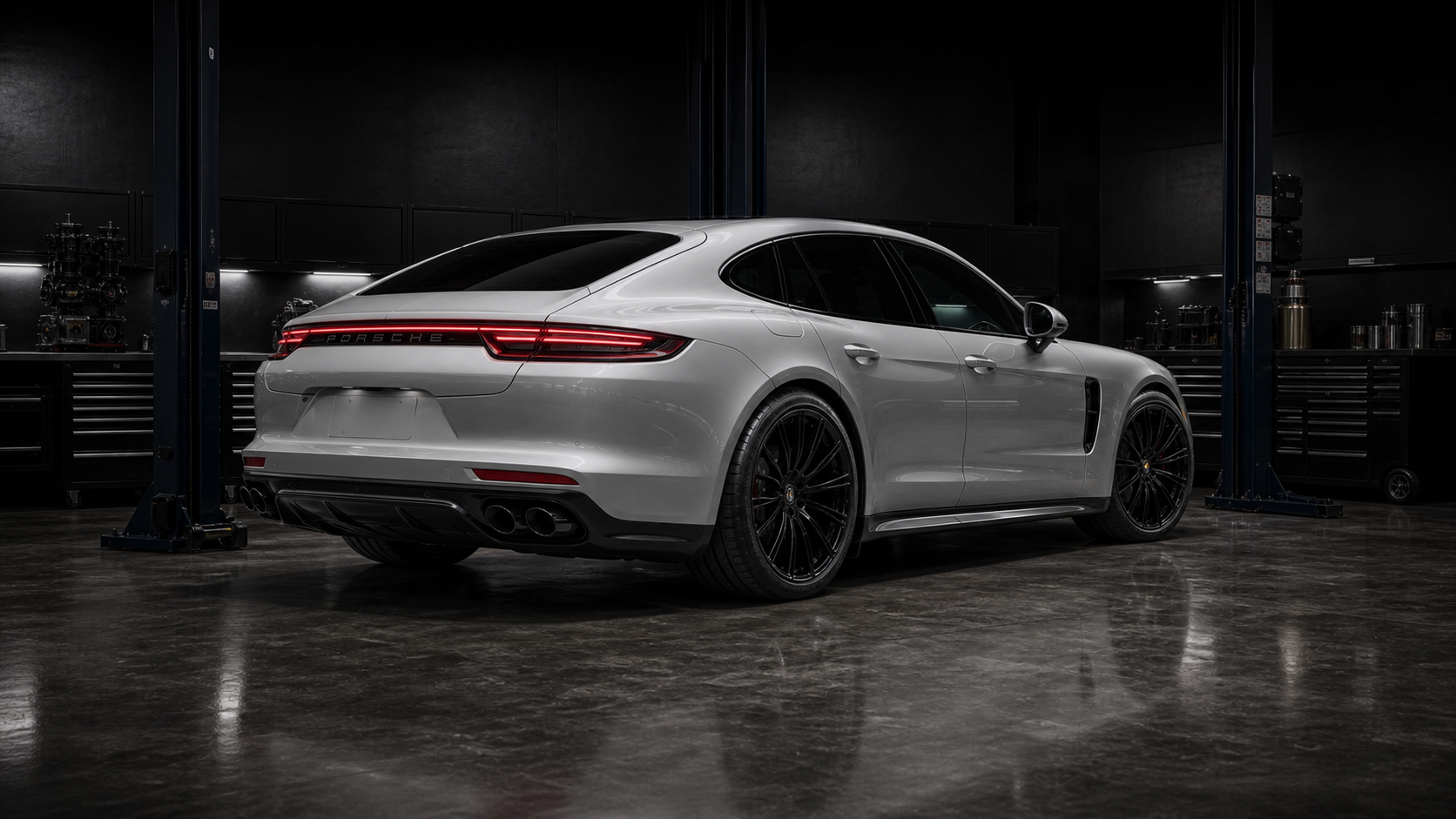 Silver Porsche Panamera-style sedan inside a dark QMSPORTS shop bay