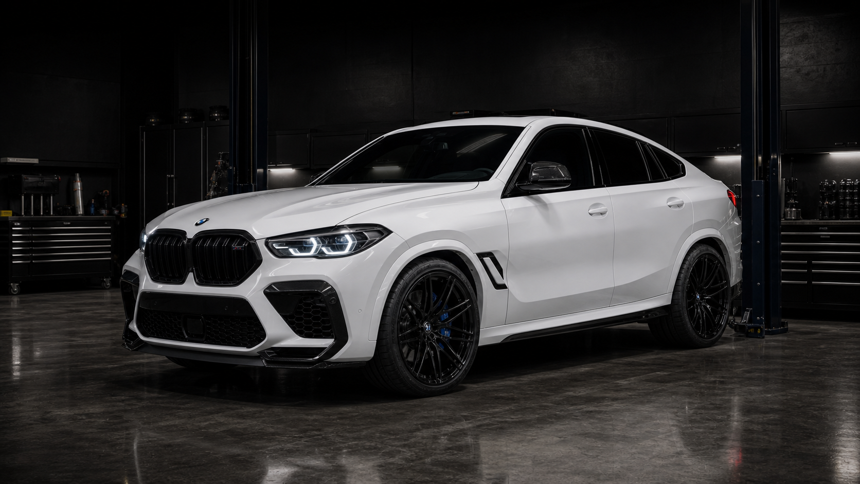 White BMW X6 M-style SUV inside a dark QMSPORTS shop bay